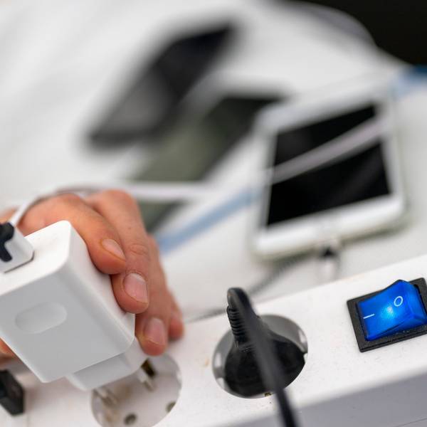 Ein Mann zieht den Stecker eines Ladegeräts für ein Smartphone aus einer Steckdosenleiste.