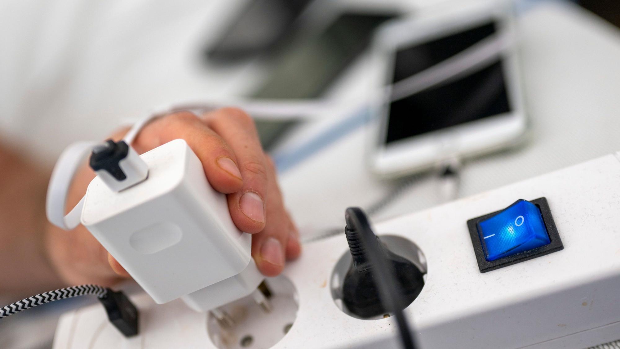 Ein Mann zieht den Stecker eines Ladegeräts für ein Smartphone aus einer Steckdosenleiste.
