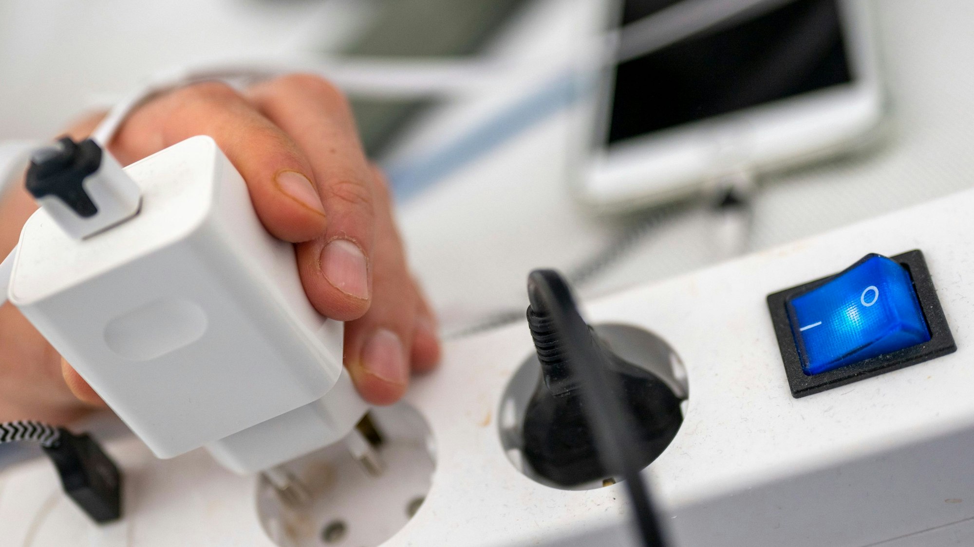 Ein Mann zieht den Stecker eines Ladegeräts aus einer Steckdosenleiste.