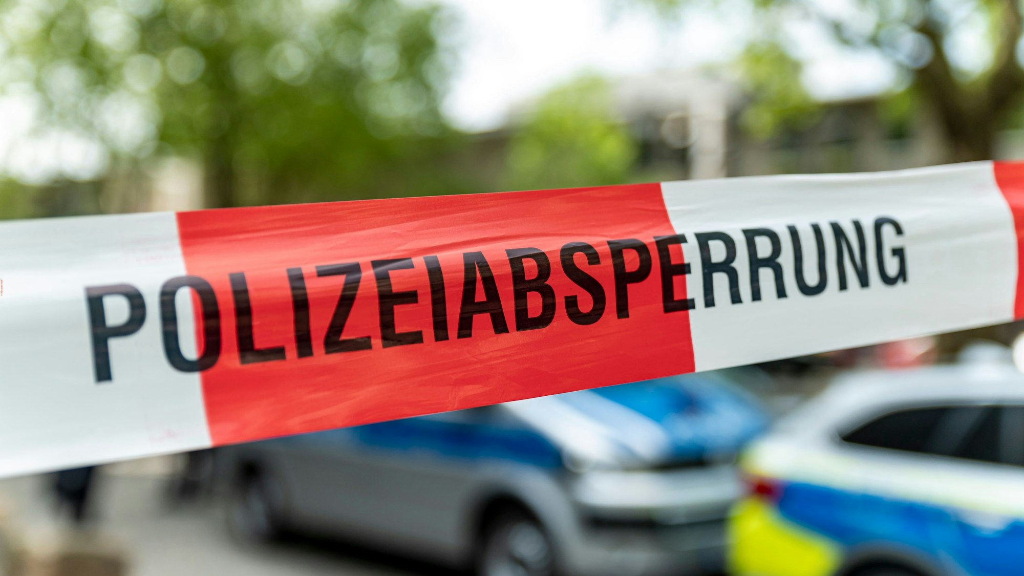 Auf rot-weißem Flatterband steht das Wort „Polizeiabsperrung“. Dahinter stehen einige Polizeiwagen.