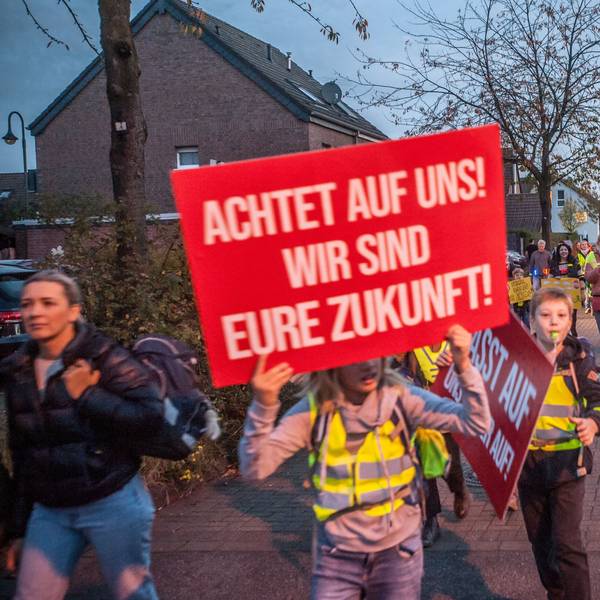 Kinder mit Plakaten und in elterlicher Begleitung protestieren in der Dämmerung auf der Hitdorfer Ringstraße für mehr Sicherheit