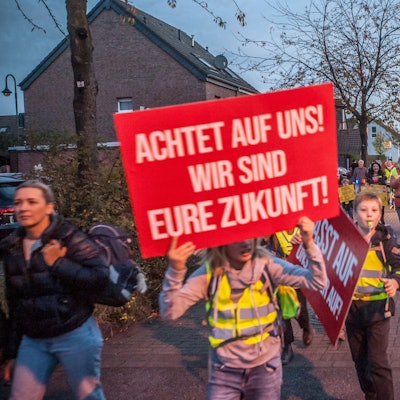 Kinder mit Plakaten und in elterlicher Begleitung protestieren in der Dämmerung auf der Hitdorfer Ringstraße für mehr Sicherheit