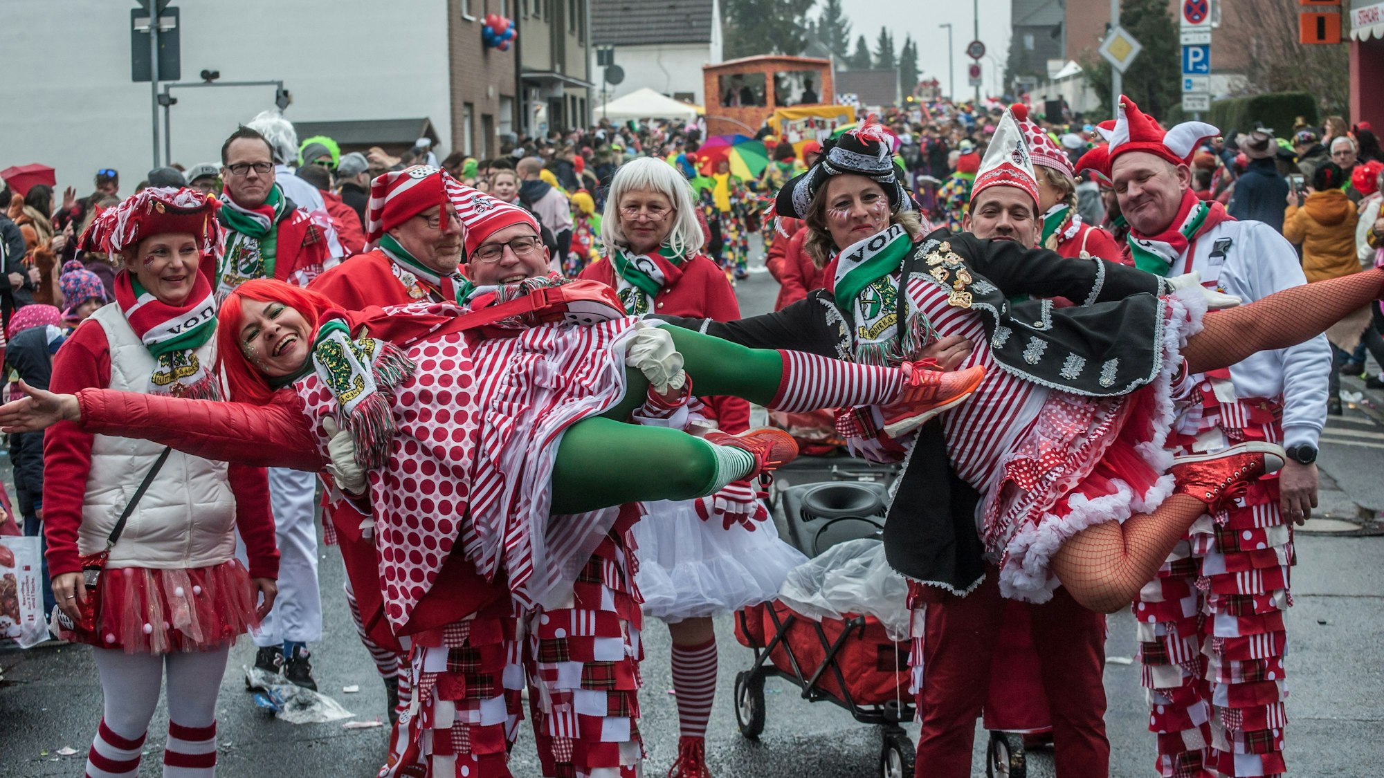 Verkleidete Männer im Karnevalszug heben zwei verkleidete Frauen elegant hoch.