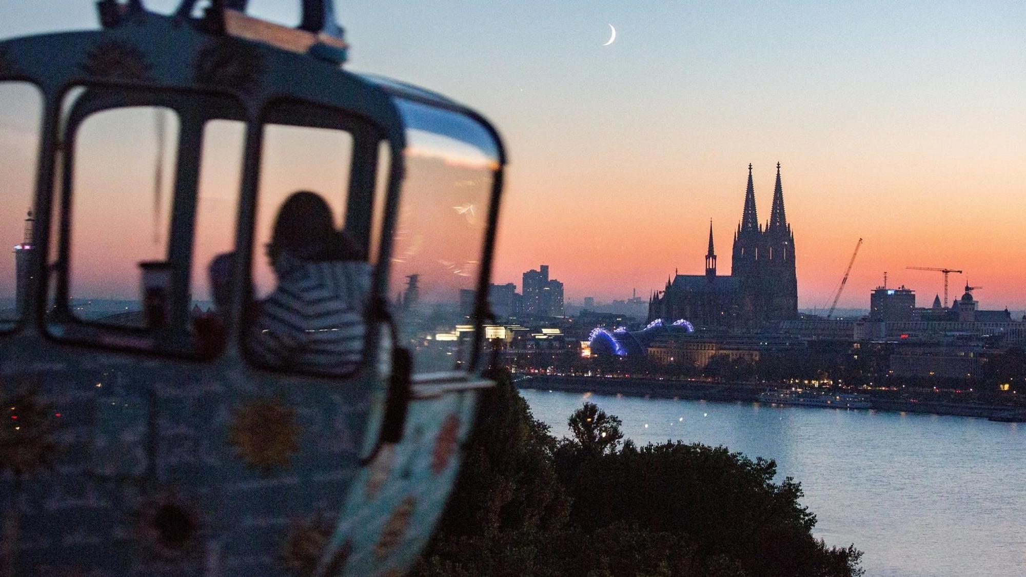 Eine Gondel der Seilbahn vor dem Köln-Panorama in der Dämmerung