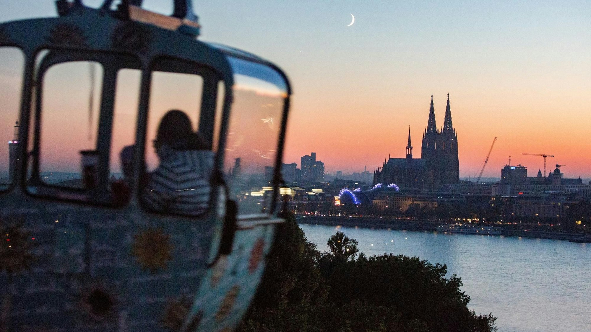 Eine Gondel der Seilbahn vor dem Köln-Panorama in der Dämmerung
