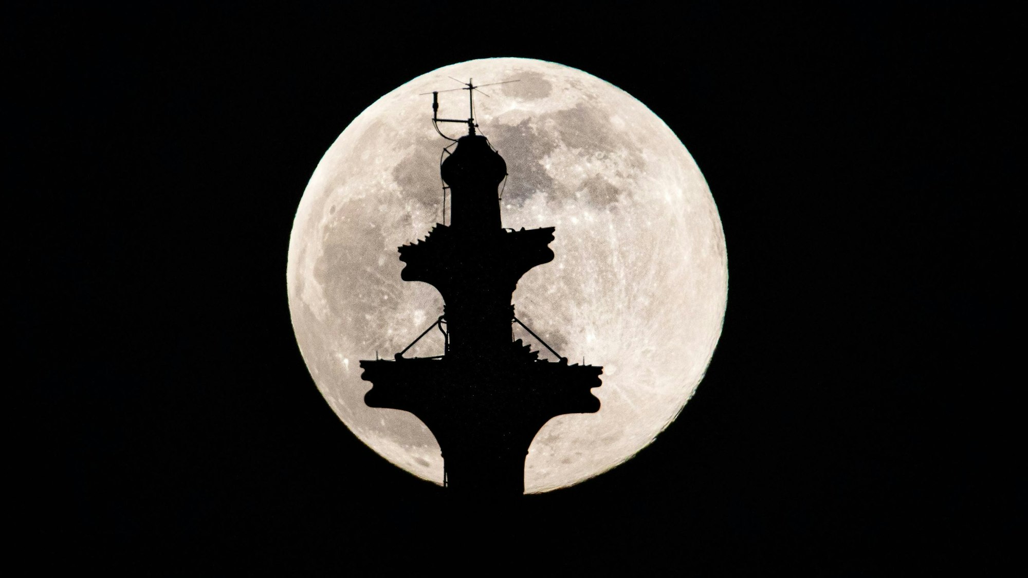 Der Mond steht als sogenannter Supermond hinter der Kreuzblume des Nordturm des Kölner Dom (Hohe Domkirche St. Petrus) am Himmel.