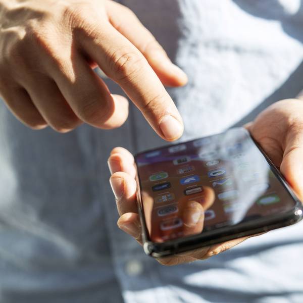 Ein Mensch hält ein Smartphone in der linken Hand und tippt mit der rechten darauf herum.