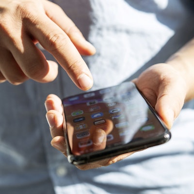 Ein Mensch hält ein Smartphone in der linken Hand und tippt mit der rechten darauf herum.