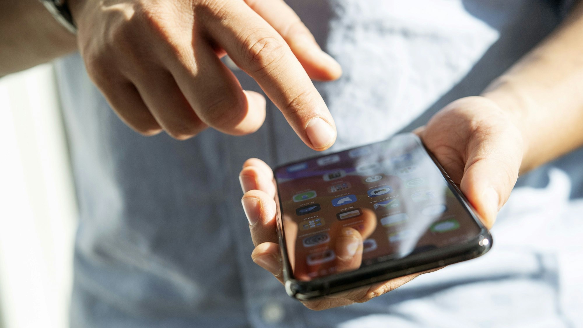 Ein Mensch hält ein Smartphone in der linken Hand und tippt mit der rechten darauf herum.