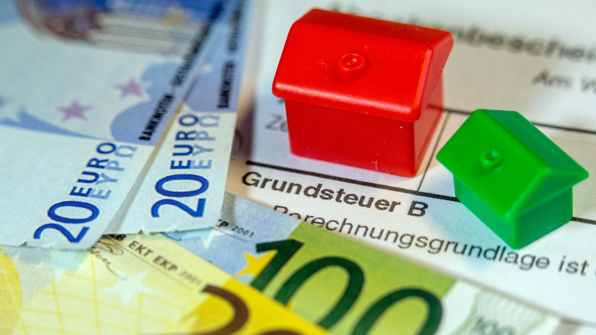 Zwei Spielzeughäuser und die Nachbildung von Euro-Geldscheinen liegen auf einem Abgabenbescheid für die Entrichtung der Grundsteuer. Symbolbild.