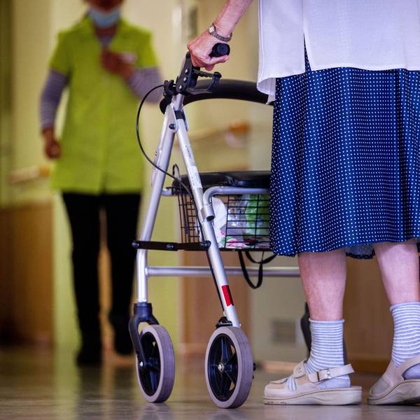 Eine Bewohnerin ist mit ihrem Rollator auf dem Flur eines Alten- und Pflegeheims unterwegs.