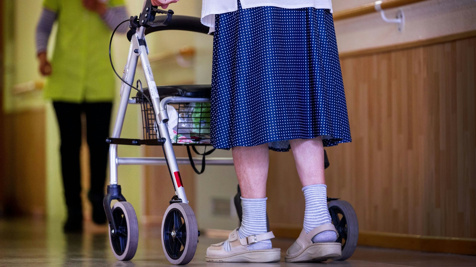 Eine Bewohnerin ist mit ihrem Rollator auf dem Flur eines Alten- und Pflegeheims unterwegs.