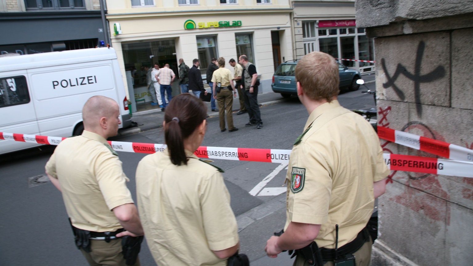 Drei Polizisten stehen hinter der Absperrung vor der Salatbar in der Gertrudenstraße in der Kölner Innenstadt, wo Anke Schäfer im Jahr 2007 ermordet wurde