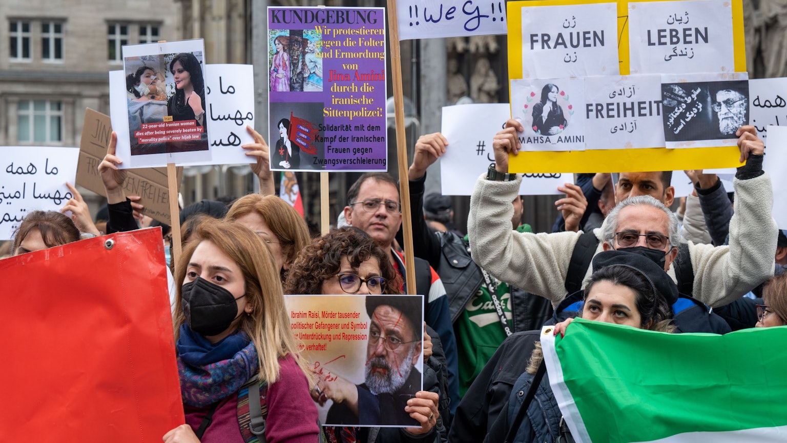 Iranerinnen und Iraner stehen mit Protest-Plakate vor dem Kölner Dom.