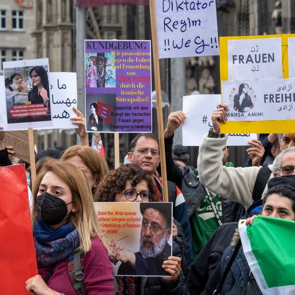 Iranerinnen und Iraner stehen mit Protest-Plakate vor dem Kölner Dom.