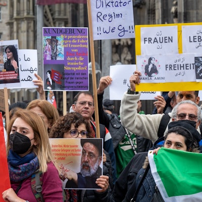 Iranerinnen und Iraner stehen mit Protest-Plakate vor dem Kölner Dom.