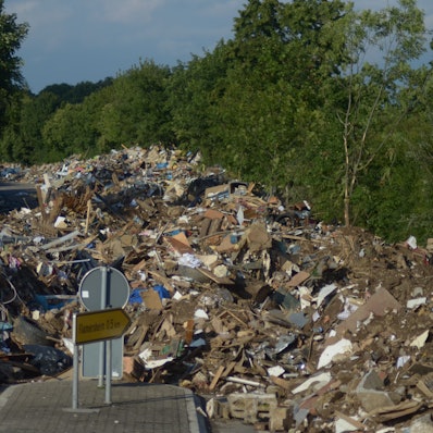 Große Mengen von Flutsperrmüll liegen auf einer von Bäumen gesäumten Straße.