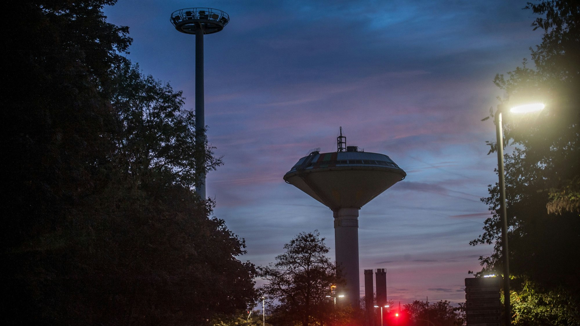 Eine ein- und eine abgeschaltete Straßenlaterne an der Olof-Palme-Straße, mit dem Wasserturm im Hintergrund.