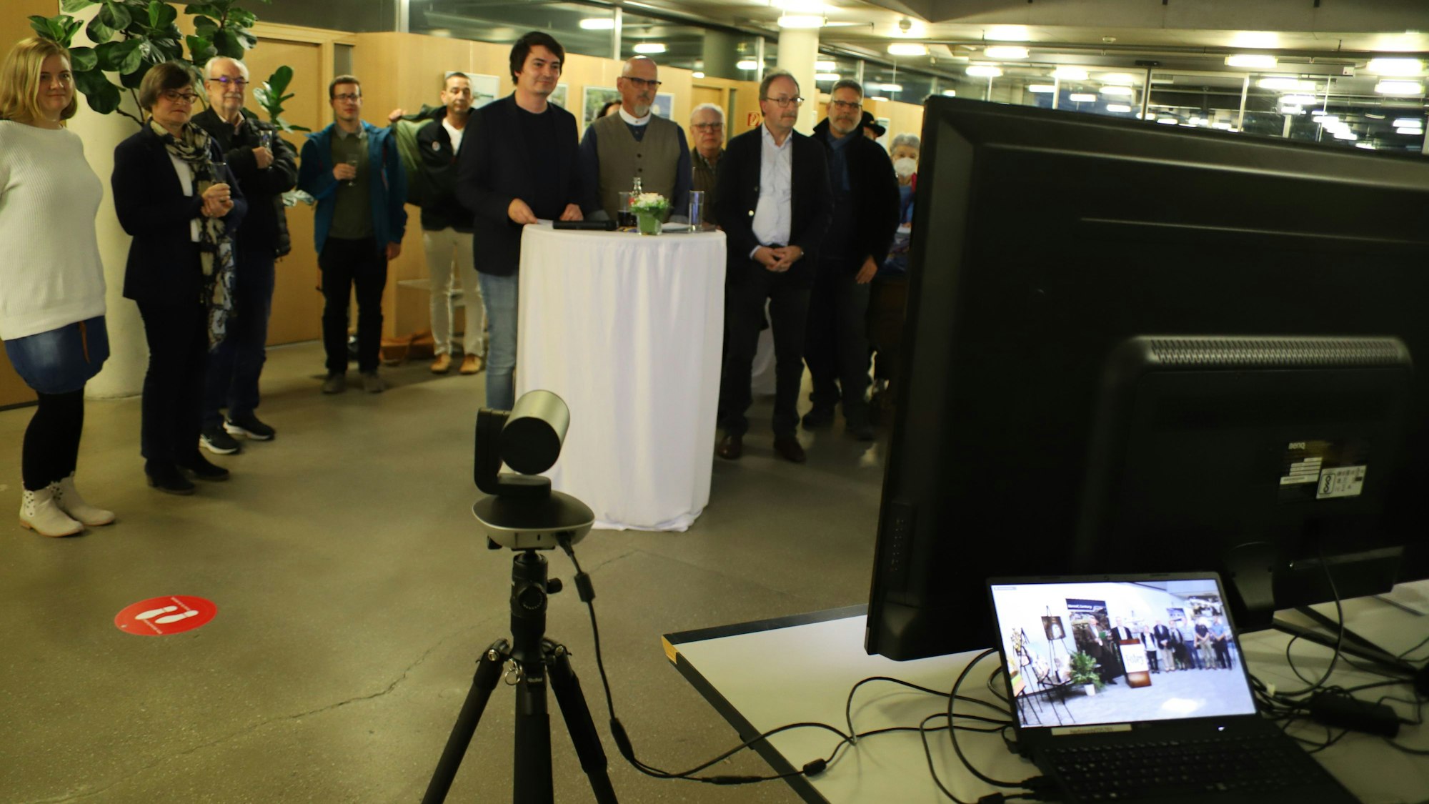 Bürgermeister Mario Dahm steht mit mehreren Vertreterinnen und Vertretern vor einem Bildschirm. Auf einem Laptop ist die Übertragung aus Foley zu sehen.