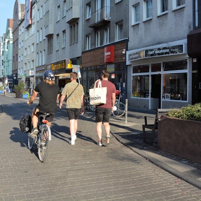 Ein Radfahrer und zwei Fußgänger laufen nebeneinander auf der Deutzer Freiheit.