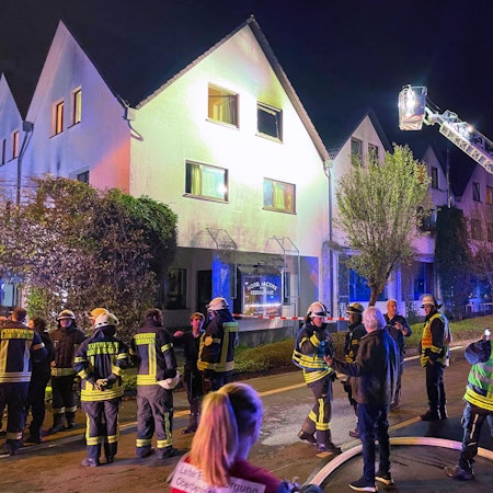 Zahlreiche Feuerwehrleute stehen vor dem Hotel Jacobs, im Hintergrund ist ein Feuerwehrwagen mit Drehleiter zu sehen.