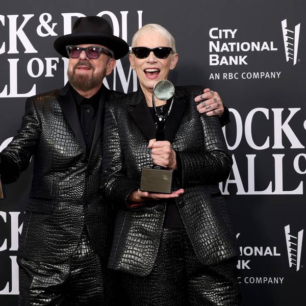 Dave Stewart und Annie Lennox bei der Pressekonferenz mit den Statuen der „Rock and Roll Hall of Fame“. Sie tragen schwarze Anzüge.