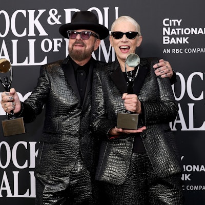 Dave Stewart und Annie Lennox bei der Pressekonferenz mit den Statuen der „Rock and Roll Hall of Fame“. Sie tragen schwarze Anzüge.