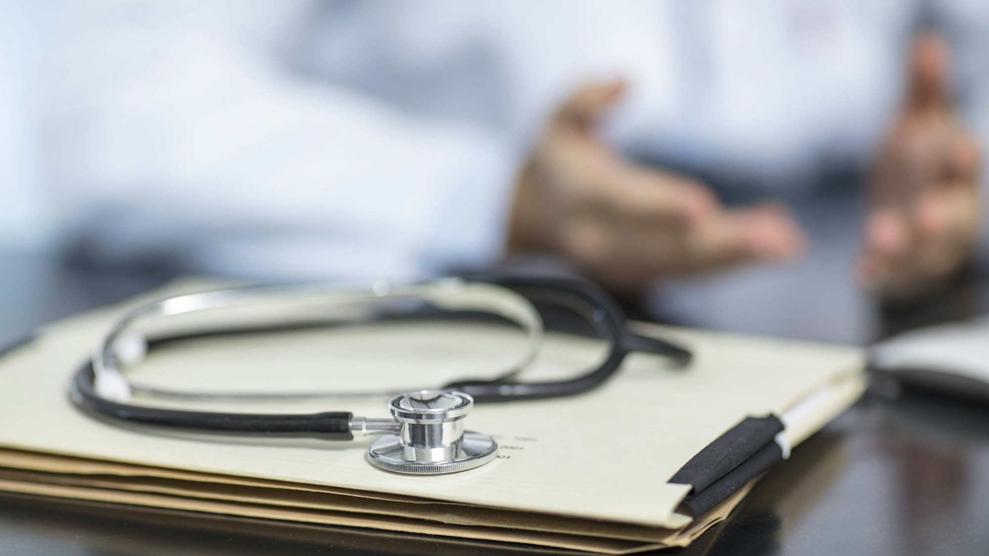 Patientenakte und Stetoskop auf dem Schreibtisch einer Arztpraxis.