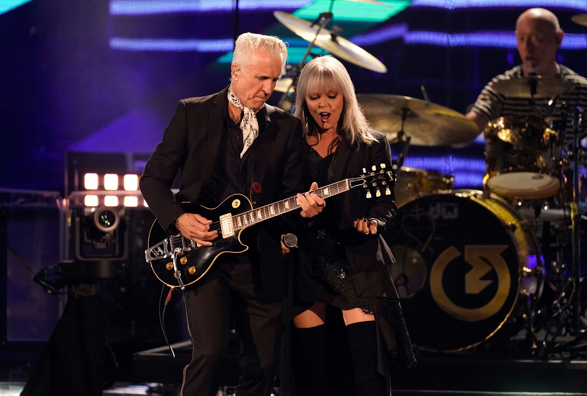 Nick Geraldo und Pat Benatar ganz in Schwarz auf der Bühne. Er spielt Gitarre, sie steht an seiner Schulter und singt dazu.