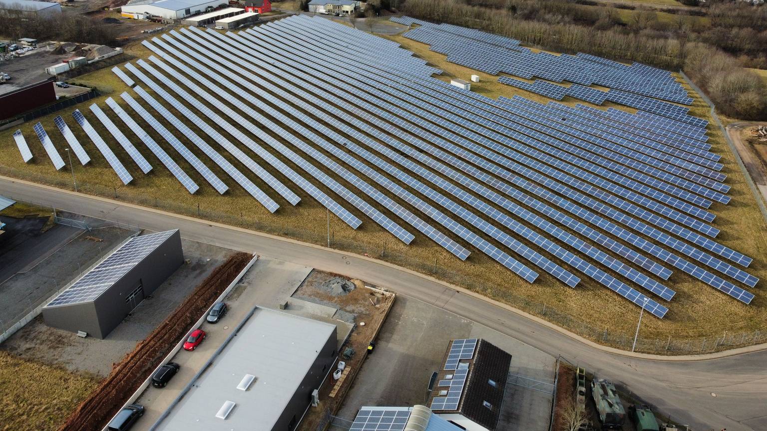Auf einer großen Fläche stehen Dutzende Solaranlagen. Im Hintergrund sind Felder zu sehen.