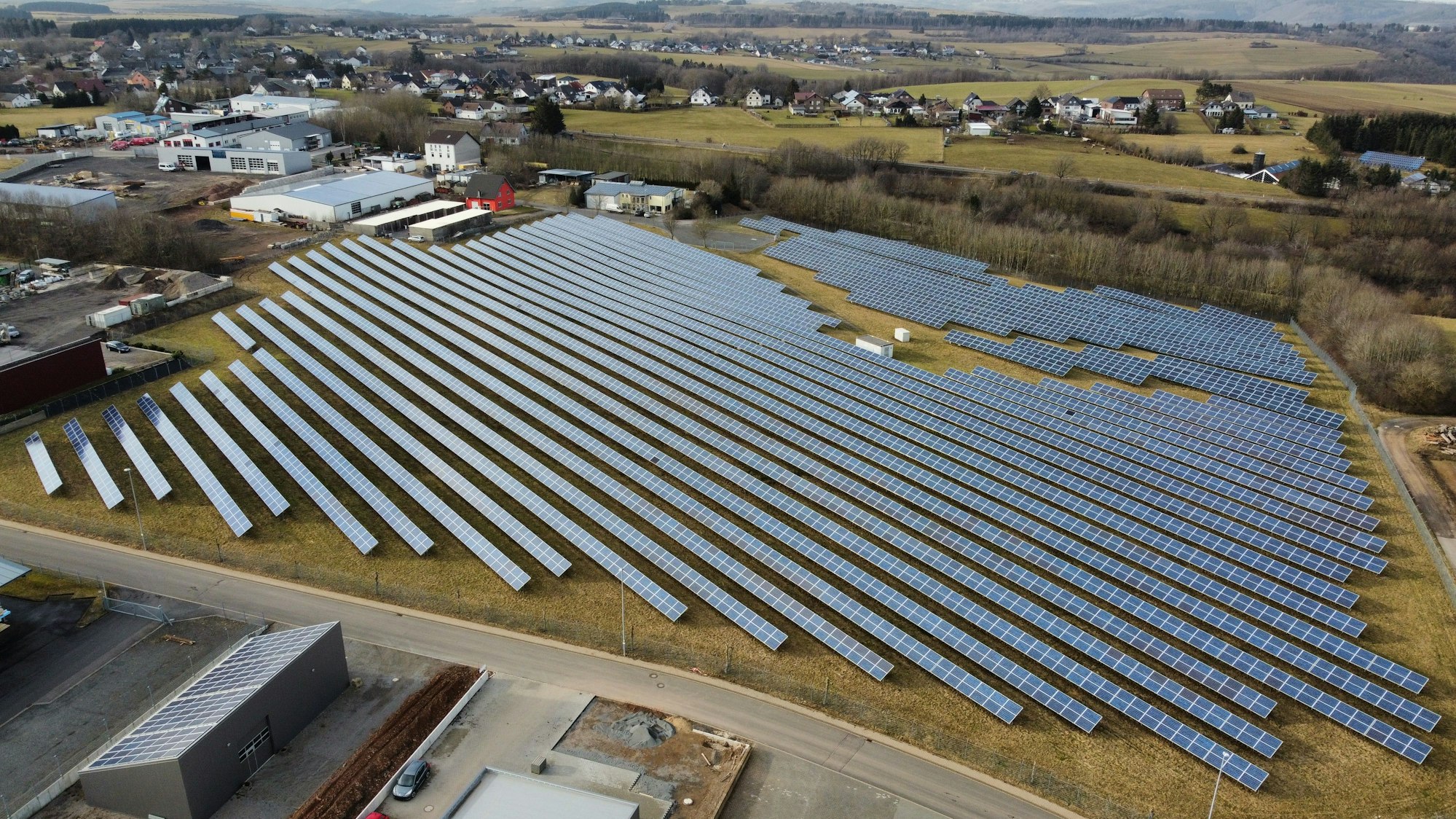 Auf einer großen Fläche stehen Dutzende Solaranlagen. Im Hintergrund sind Felder zu sehen.