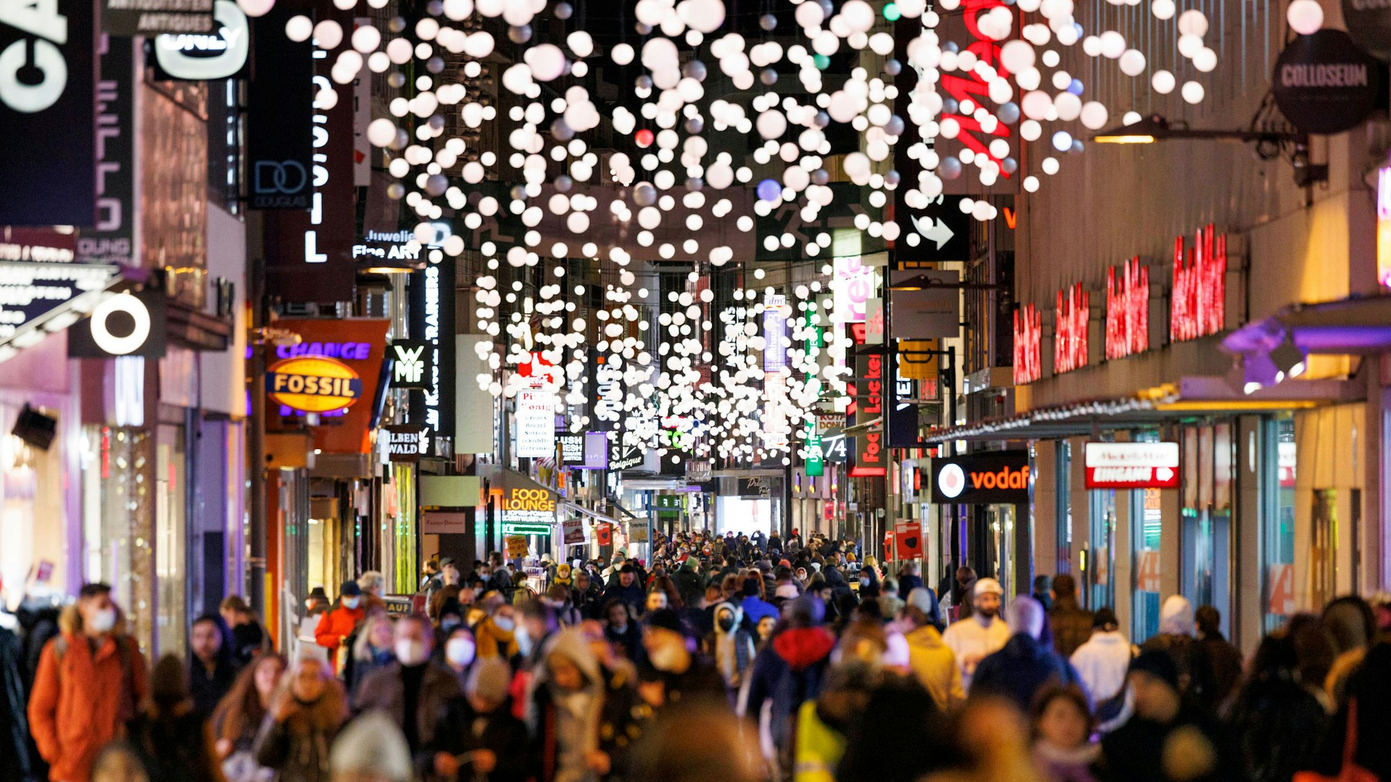 Passanten streifen durch die von Weihnachtsbeleuchtung gesäumte Hohe Straße in Köln.