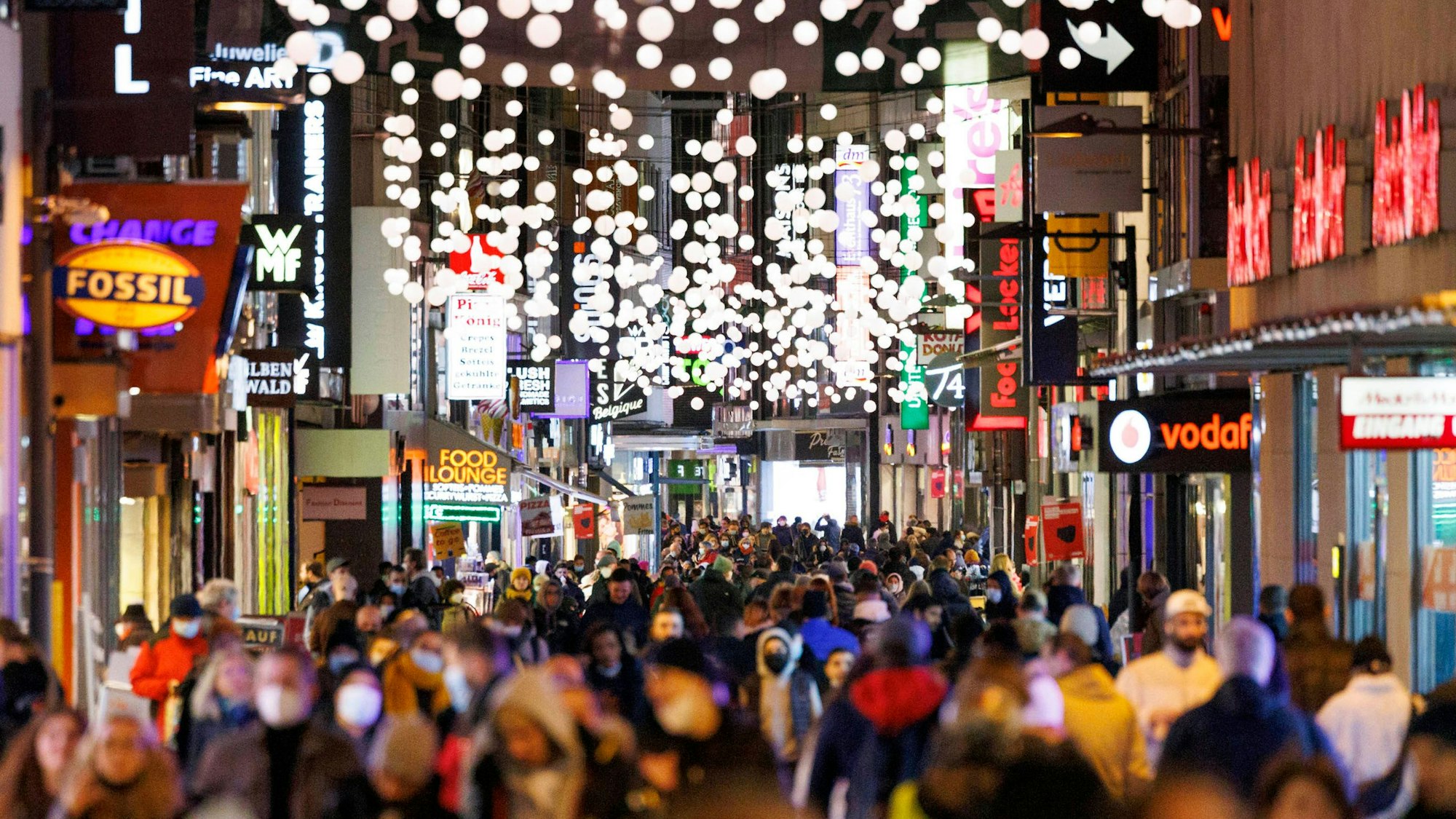 Passanten streifen durch die von Weihnachtsbeleuchtung gesäumte Hohe Straße in Köln.