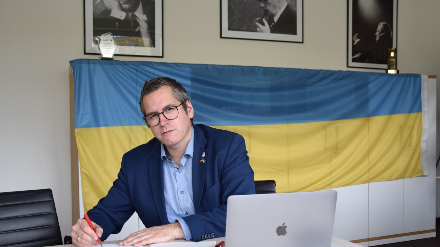 Bedburgs Bürgermeister Sascha Solbach unterzeichnet die Urkunde zur Solidaritätspartnerschaft mit Mykolajiw. Im Hintergrund ist eine Ukraine-Flagge zu sehen.