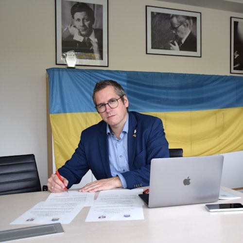 Bedburgs Bürgermeister Sascha Solbach unterzeichnet die Urkunde zur Solidaritätspartnerschaft mit Mykolajiw. Im Hintergrund ist eine Ukraine-Flagge zu sehen.