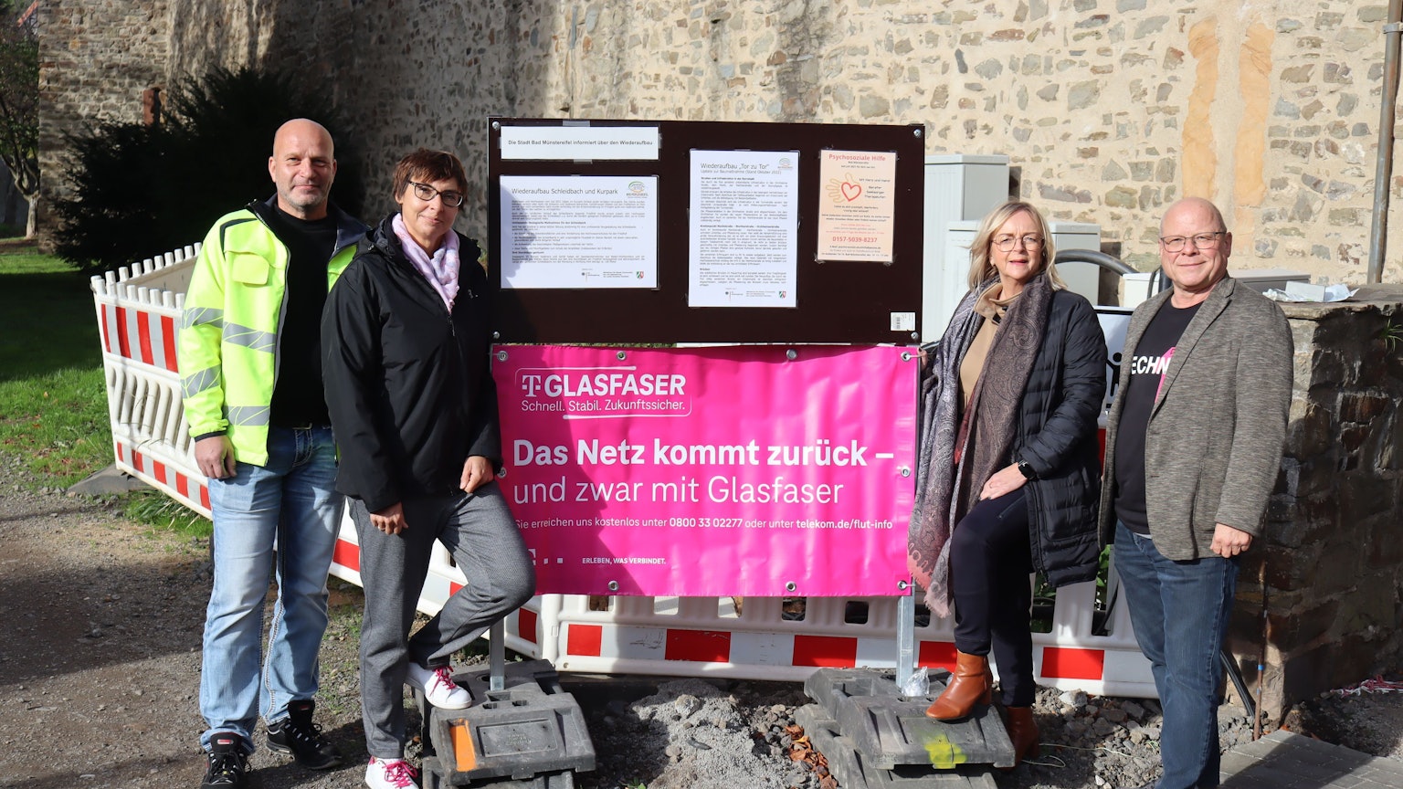Mehrere Personen stehen vor einem Schild der Telekom. Dahinter ist die Stadtmauer zu sehen.