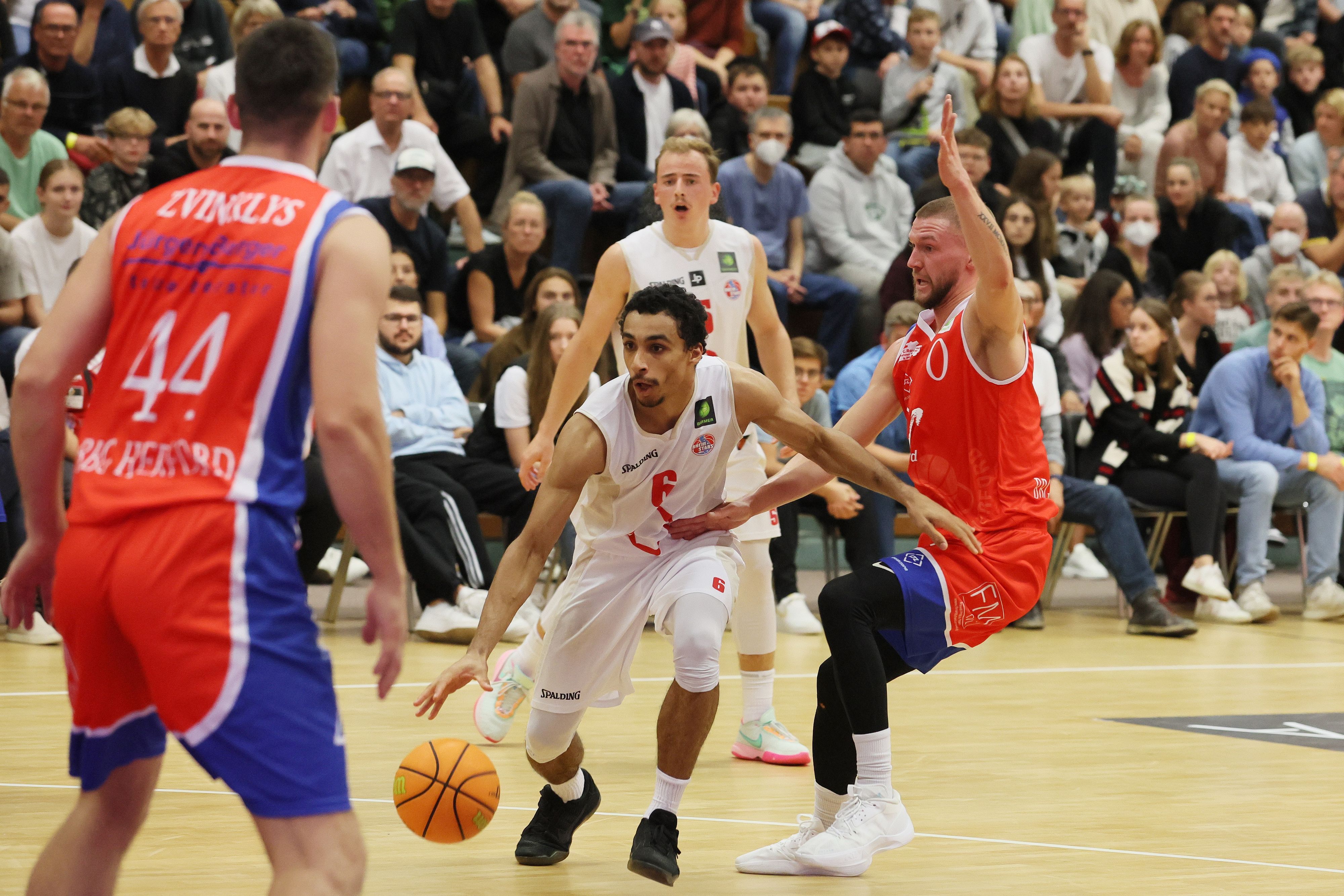 Ein Basketballer versucht, sich auf dem Weg zum Korb gegen zwei Gegenspieler durchzusetzen.