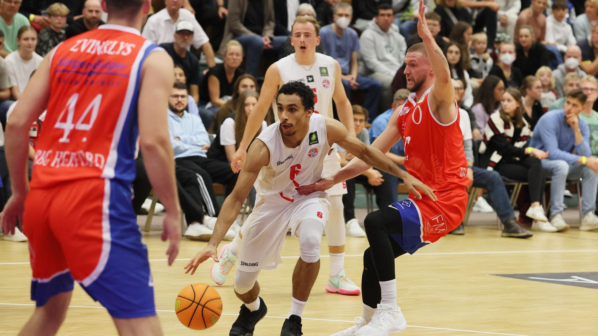 Ein Basketballer versucht, sich auf dem Weg zum Korb gegen zwei Gegenspieler durchzusetzen.