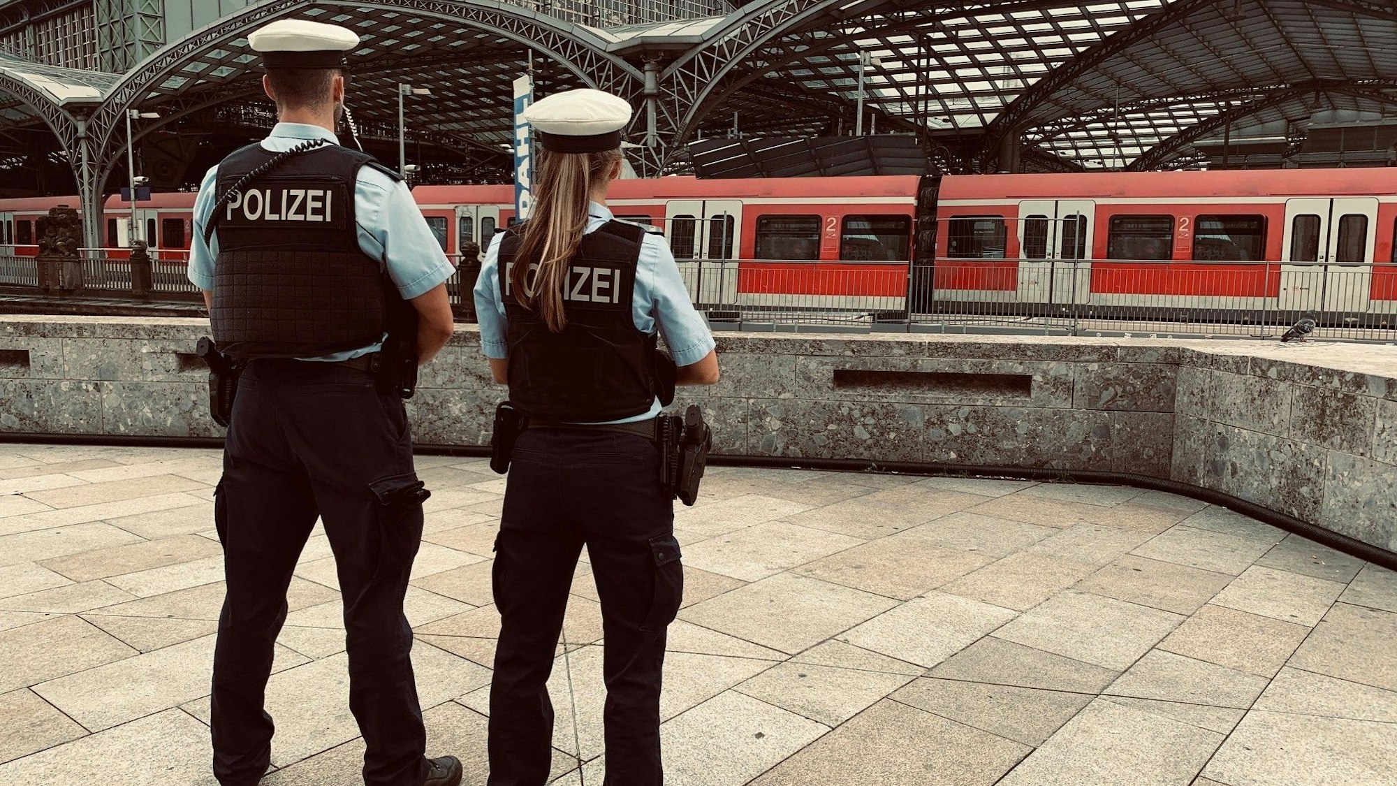 Zwei Beamte der Bundespolizei stehen am Hauptbahnhof Köln und blicken auf einen Zug.