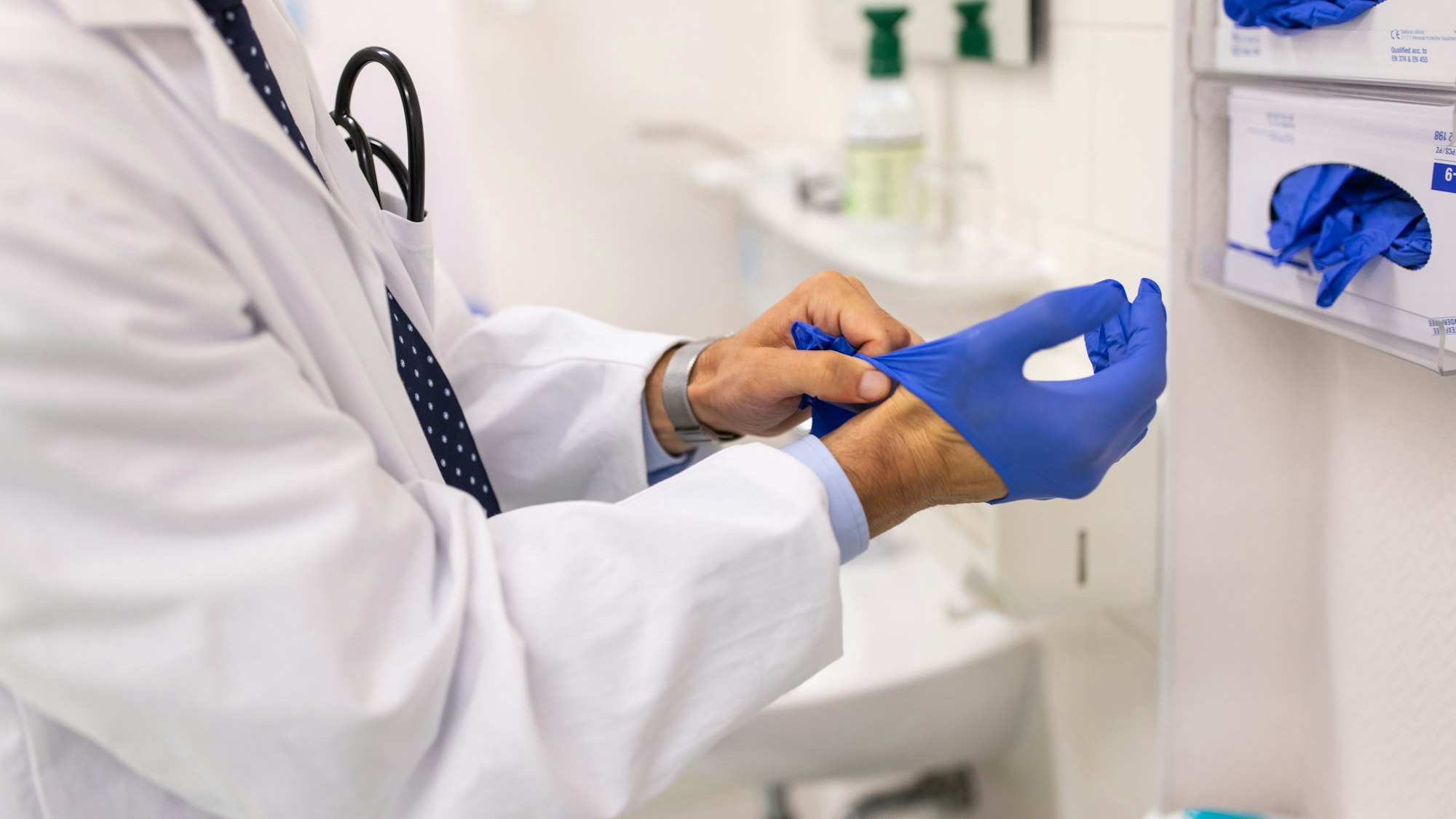 Ein Arzt zieht sich in der Praxis blaue Gummihandschuhe an.
