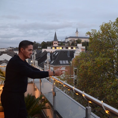 Jaroslaw Plichta blickt von seiner Wohnung im Dachgeschoss auf Bäume. Im Hintergrund sind Gebäude in Siegburg zu sehen.