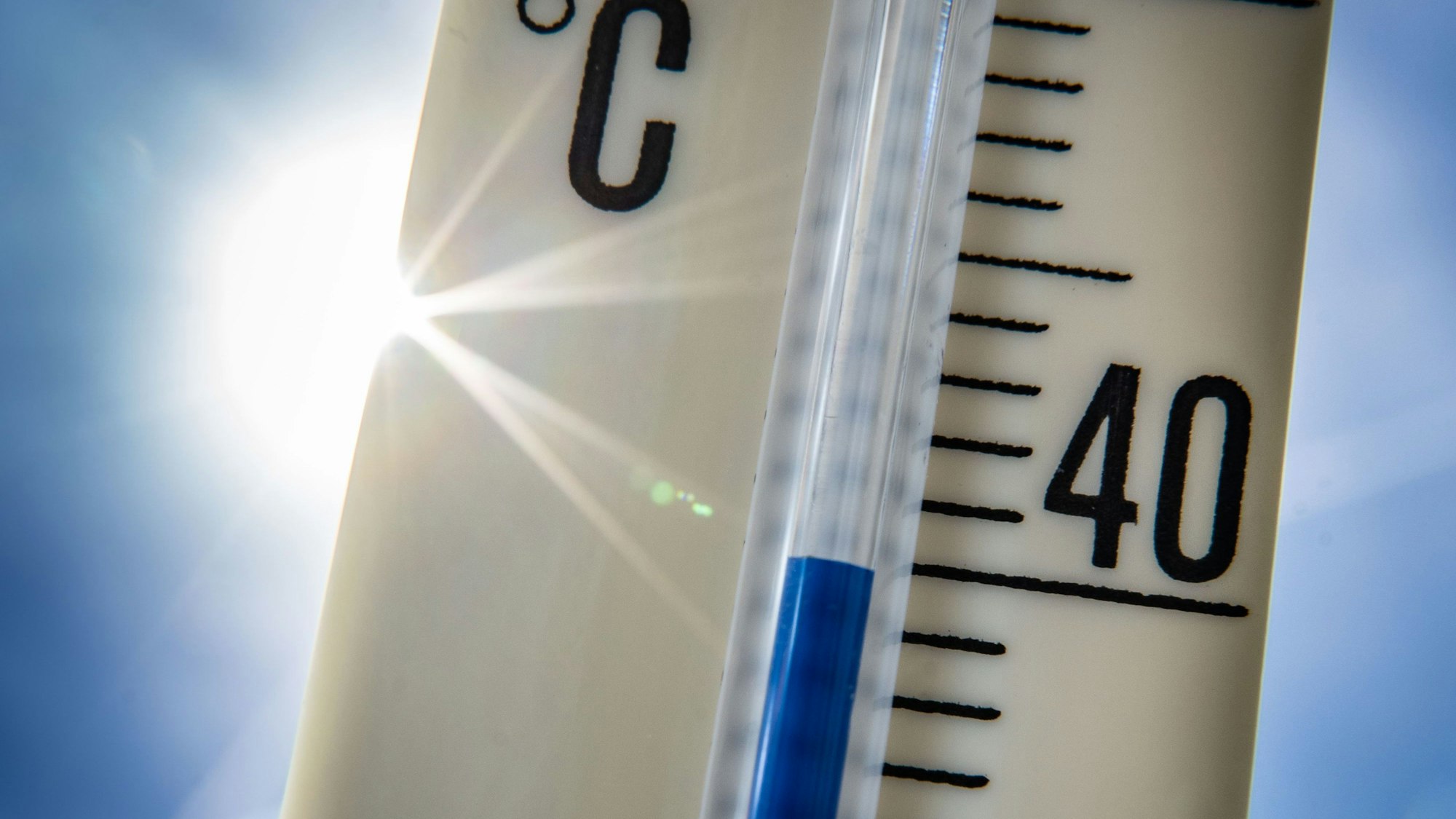 Ein Außenthermometer zeigt vor dem blauen Himmel und der Sonne eine Temperatur von nahezu 40 Grad Celsius an.
