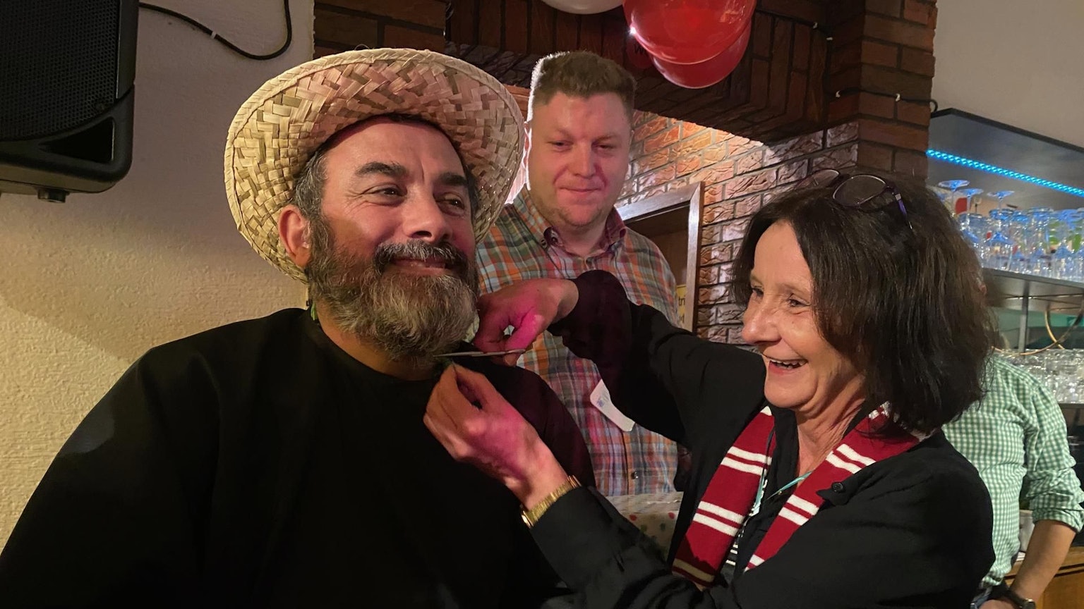 Eine Frau schneidet mit einer Schere den Bart ihres Mannes ab.