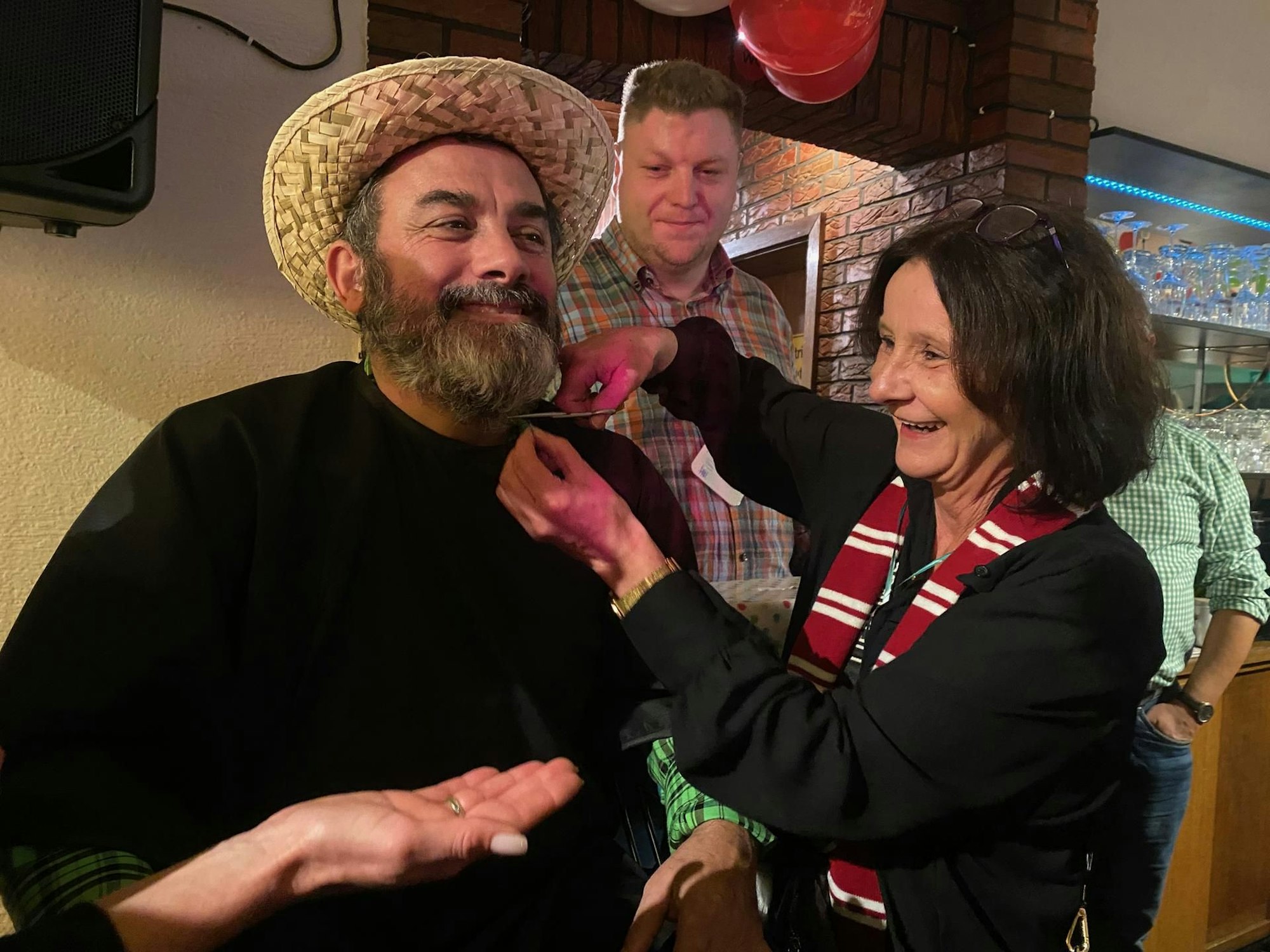 Eine Frau schneidet mit einer Schere den Bart ihres Mannes ab.