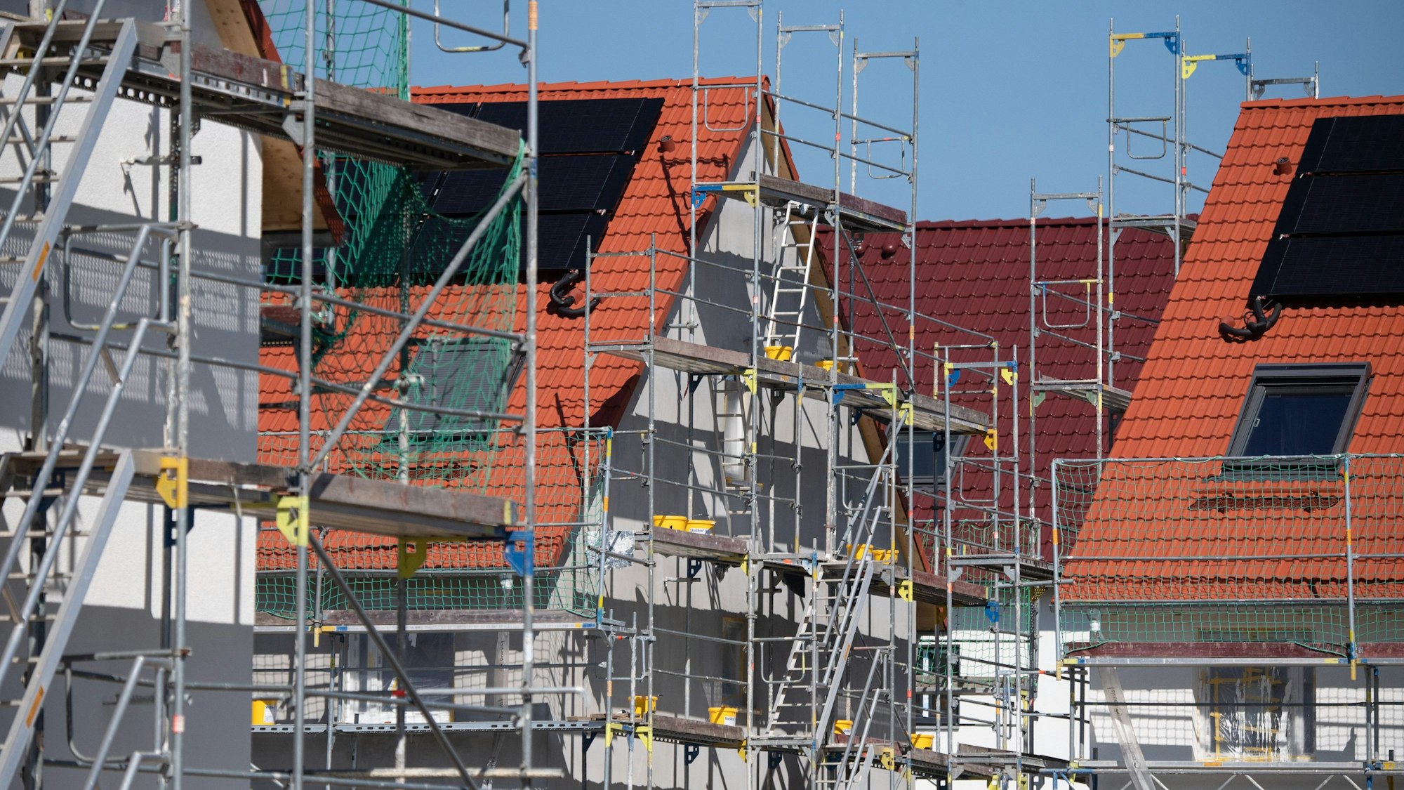 Um Häuser in einem Wohngebiet stehen mehrere Baugerüste.