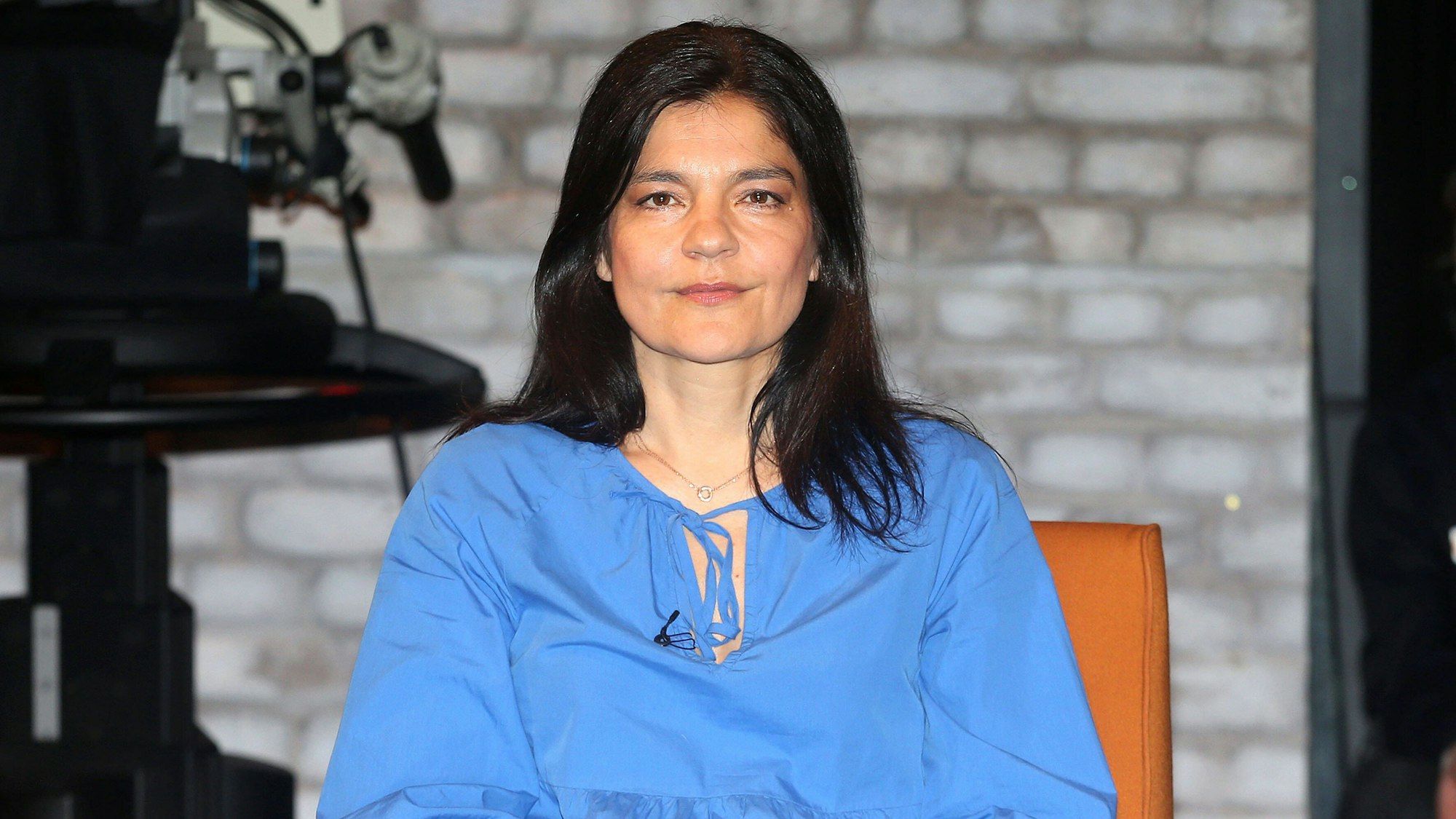 Jasmin Tabatabei sitzt auf einem Stuhl und schaut in die Kamera. Sie hat die Beine überschlagen und ihre Hände im Schoß verschränkt.