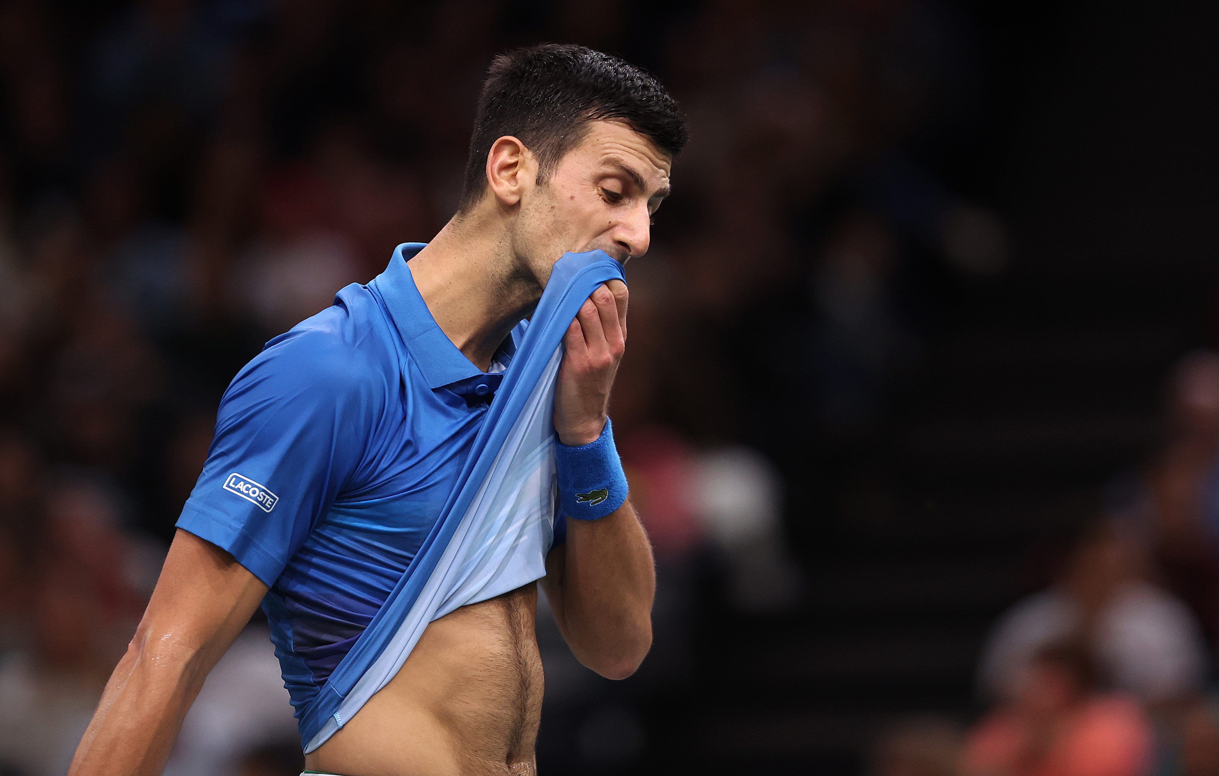 Novak Djokovic wischt sich den Mund mit seinem T-Shirt ab.