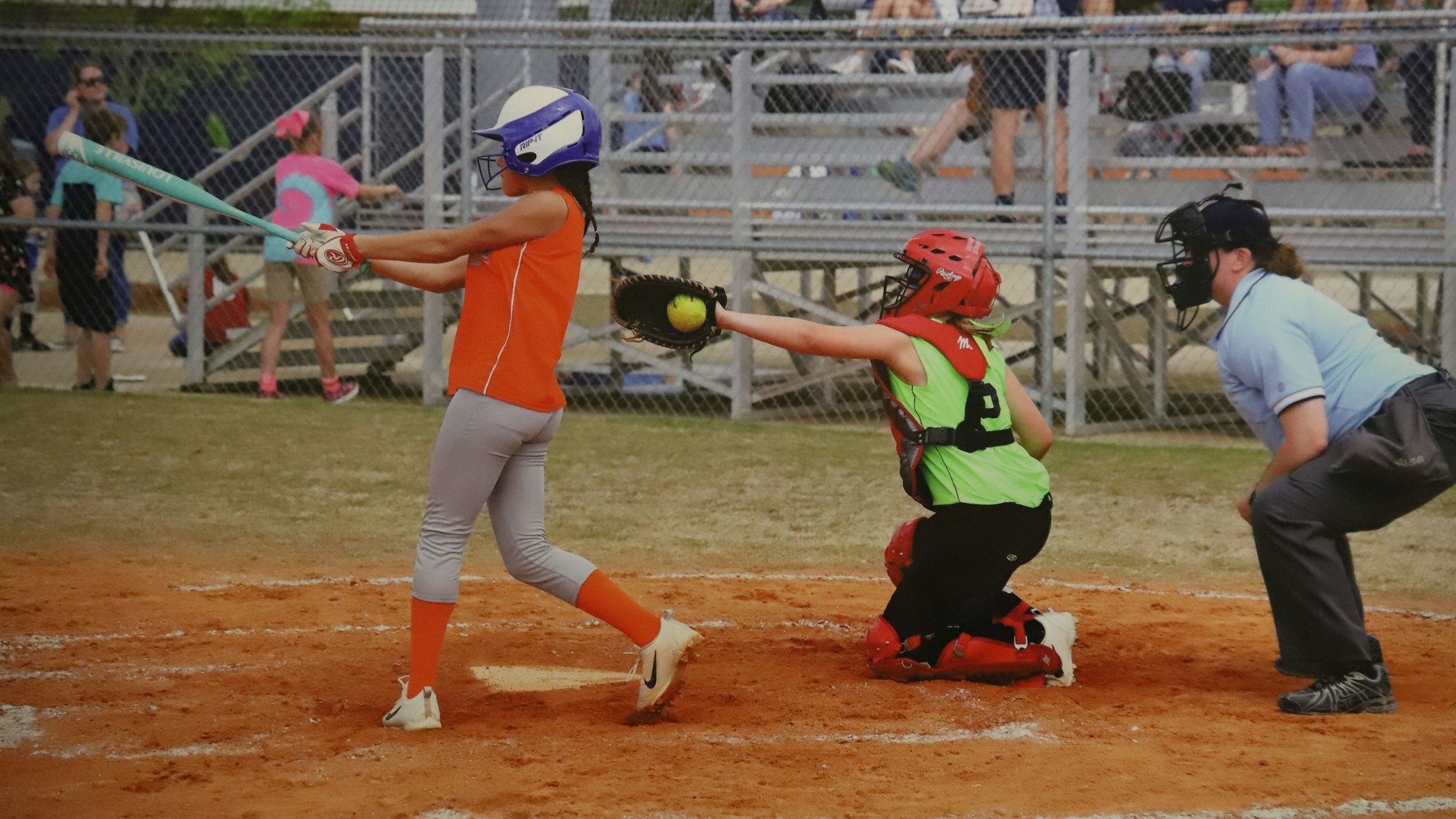Drei Personen stehen auf einem Softball-Feld und blicken in die Richtung, von der der Ball geschlagen wird.