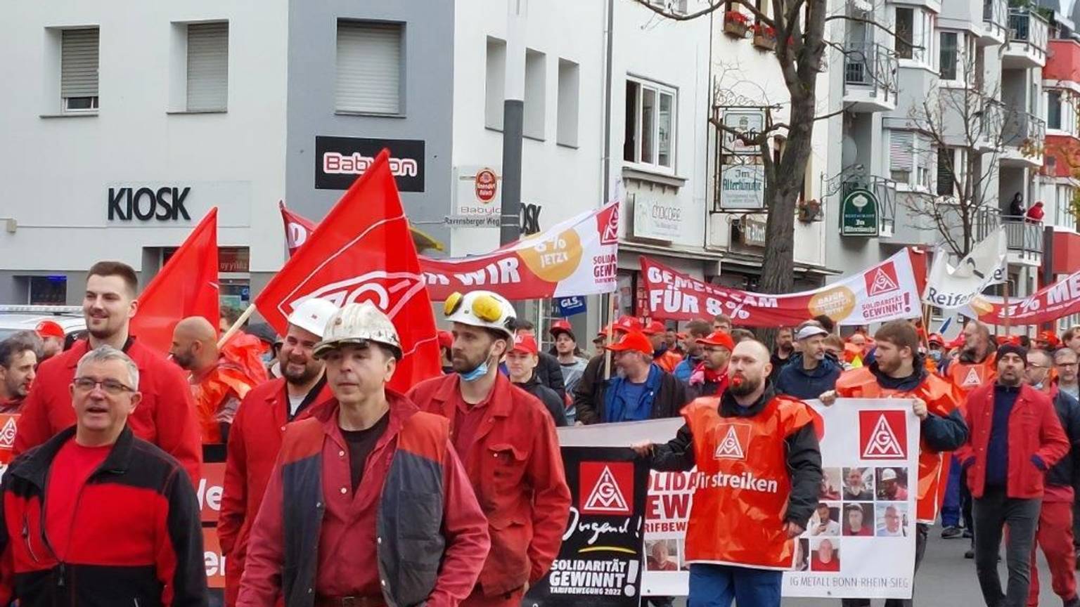 Demonstranten in roter Kleidung streiken für mehr Gehalt. Sie halten roten Fahnen in ihren Händen.