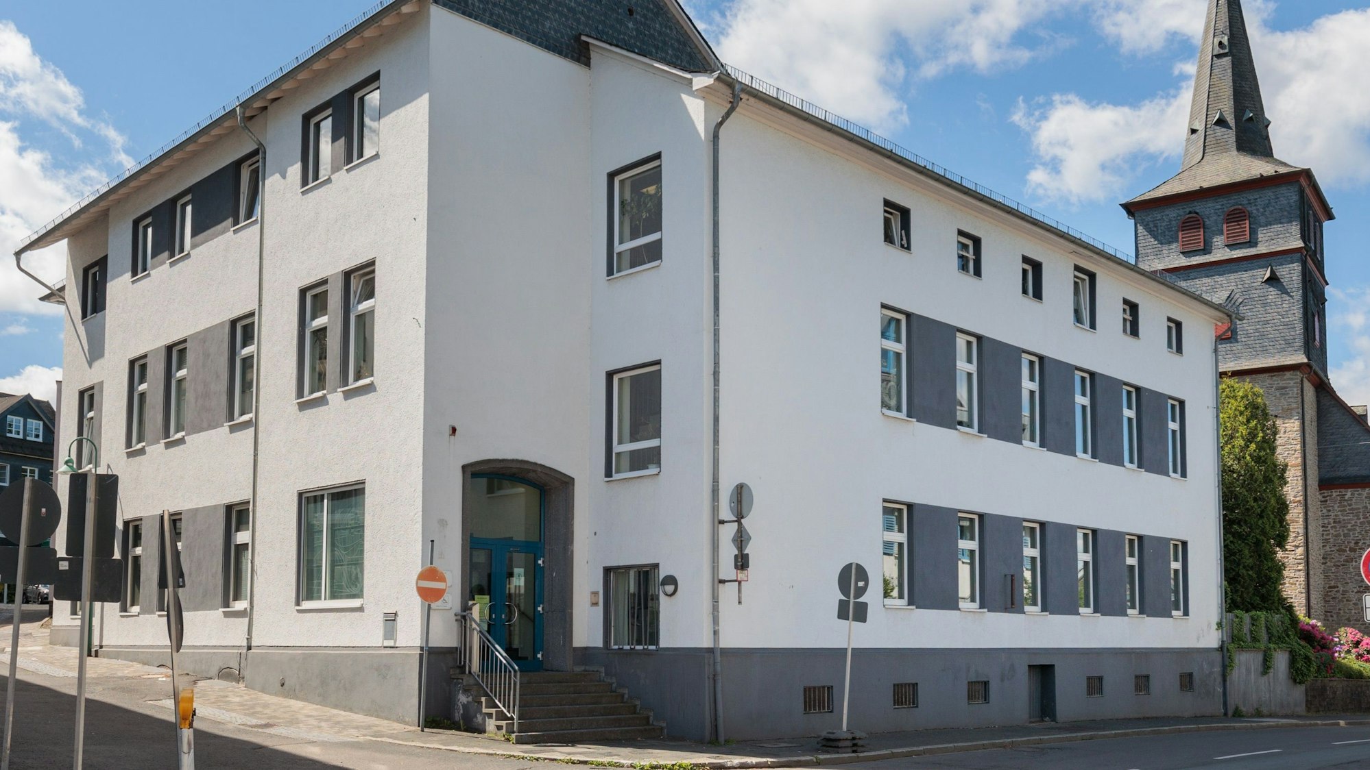 Zu sehen ist das Amtsgericht in Waldbröl, ein zweieinhalb geschossiges Gebäude, dahinter die Kirche.